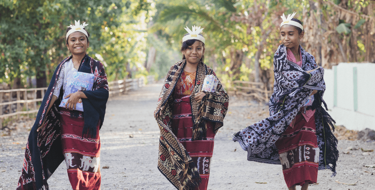 Adel, Zheane, and Gres are walking and talking on the street outside the Compassion center while holding wrapped Christmas gifts