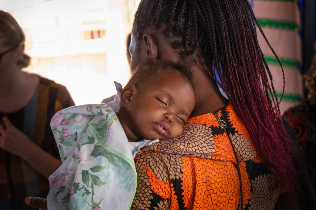 A baby sleeps on her mum's shoulder at the Baale programme