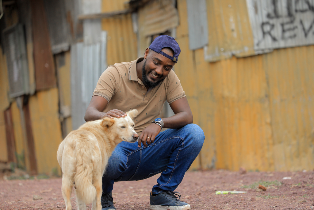 Kemi stands with a dog in front of a home reminiscent of his childhood